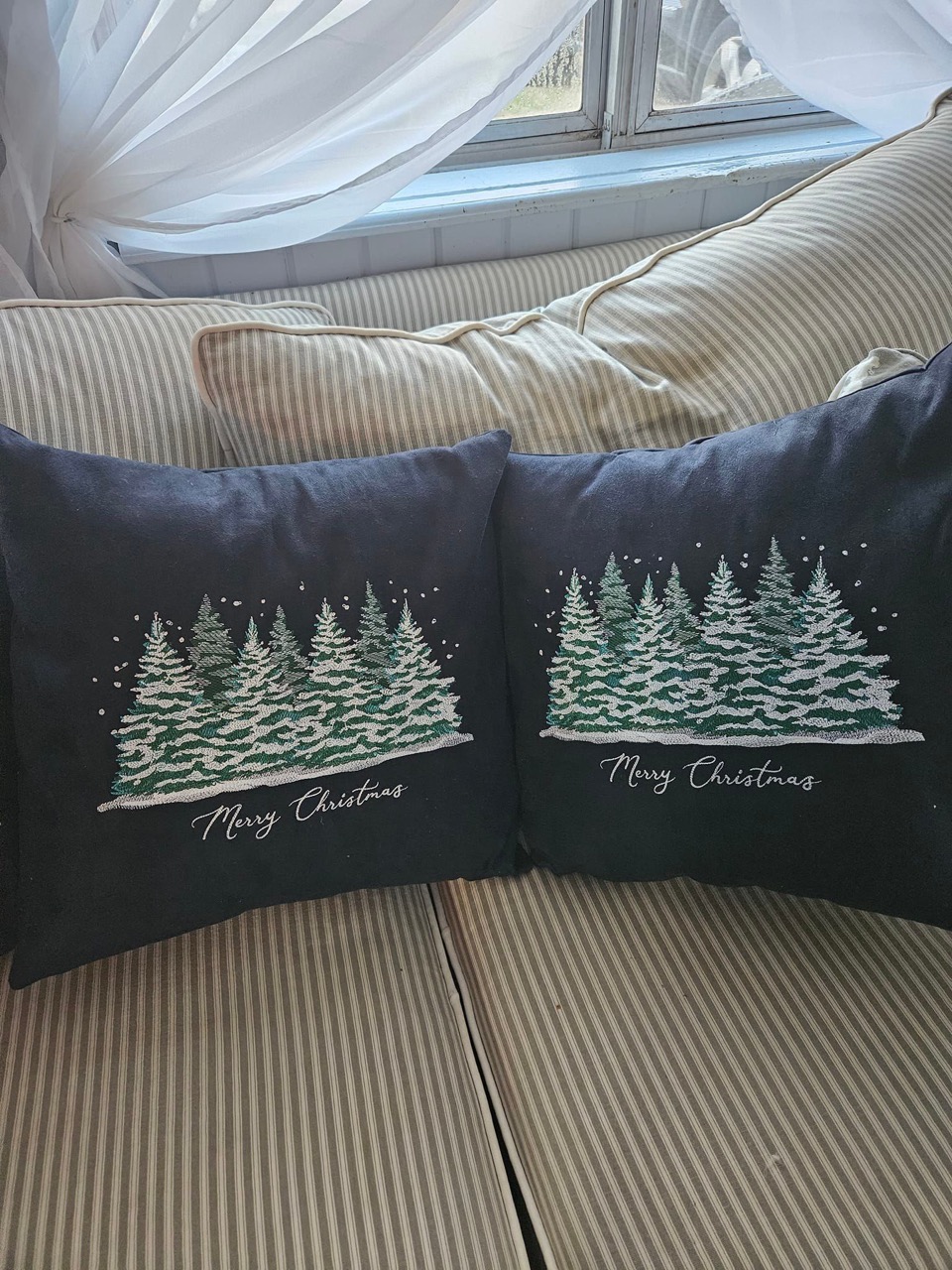 A pair of navy pillows embroidered with snowy pine trees and "Merry Christmas"