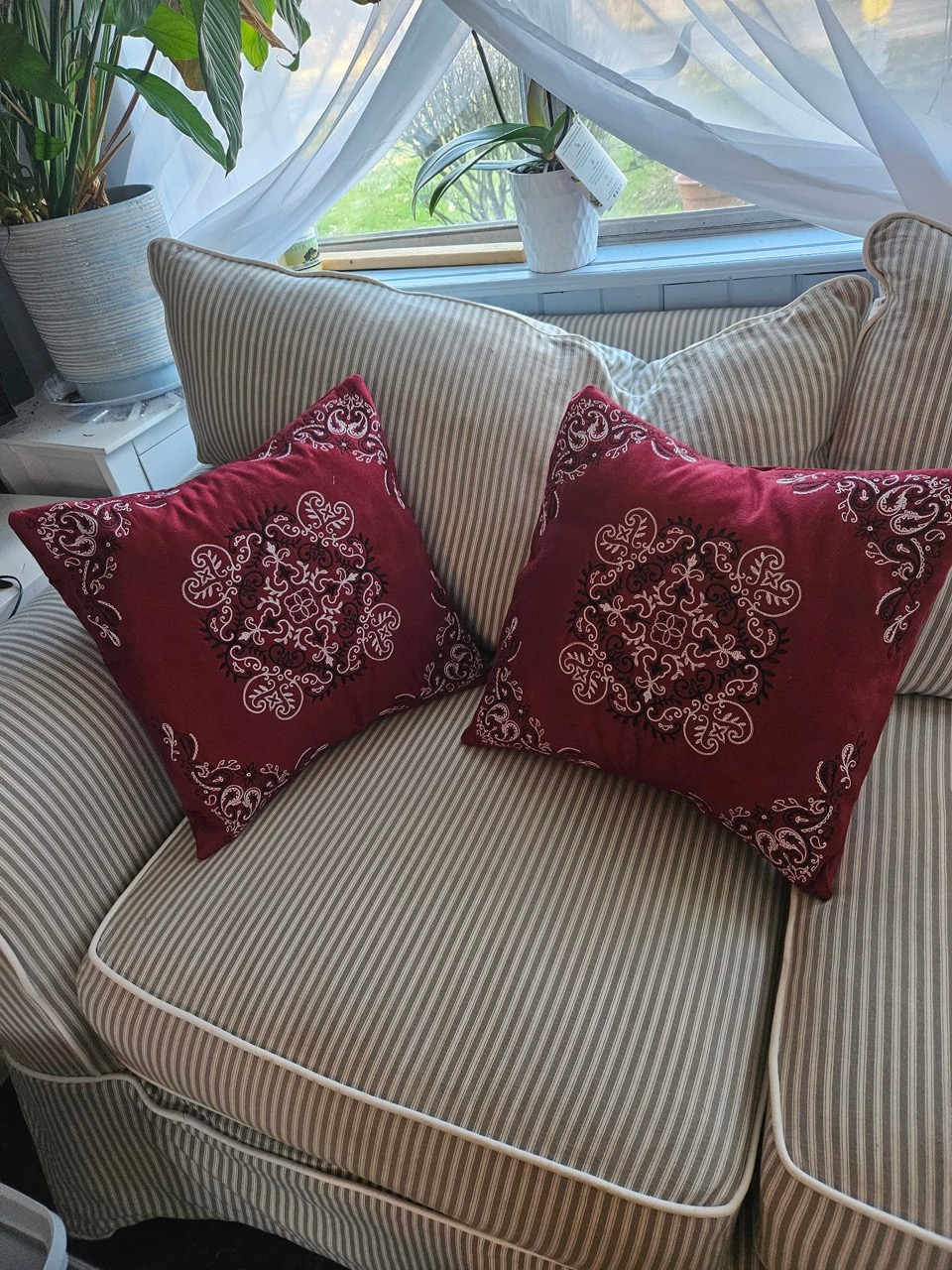 A pair of burgundy velvet pillows with ornate white embroidered medallions
