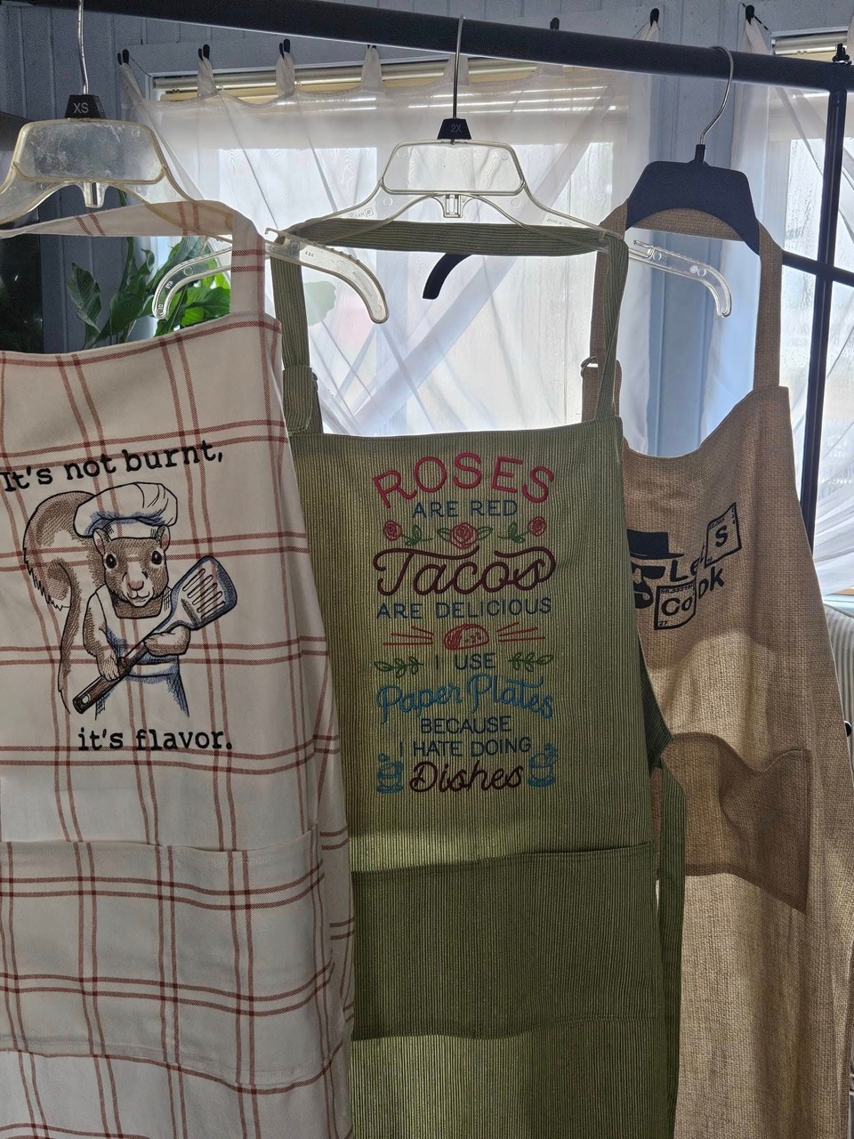 Embroidered aprons with funny sayings including "It's not burnt, it's flavor"