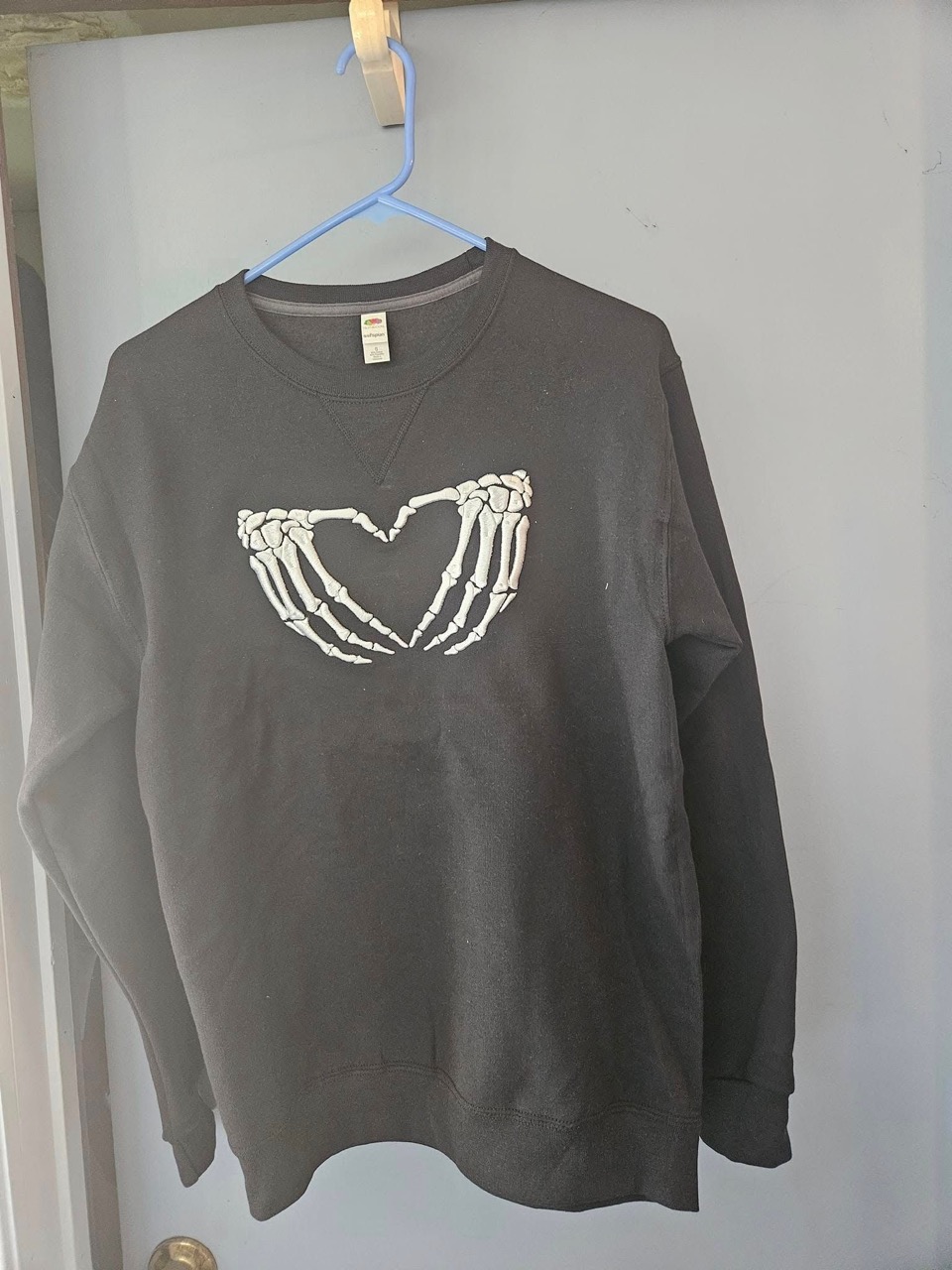 Black crewneck sweatshirt with embroidered skeleton hands forming a heart