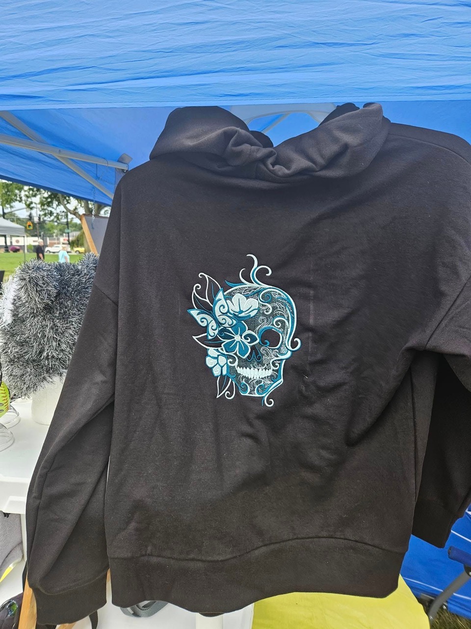 Black hoodie with a teal sugar-skull and floral embroidery on the back